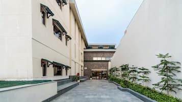 A corridor with a stone floor, a building with a traditional facade, and a small garden area with potted plants.