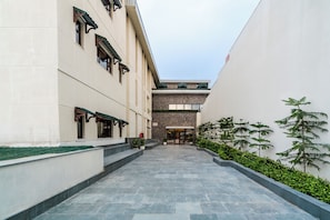 A corridor with a stone floor, a building with a traditional facade, and a small garden area with potted plants. - Aurika Naldehra Shimla (Suni)