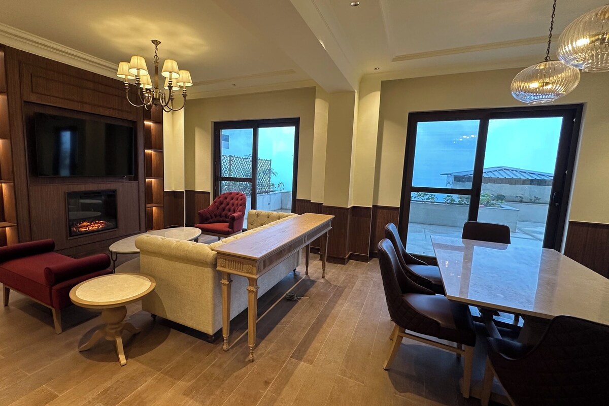 Een moderne woonkamer met een open haard, comfortabele zithoek, een eethoek en grote ramen.
