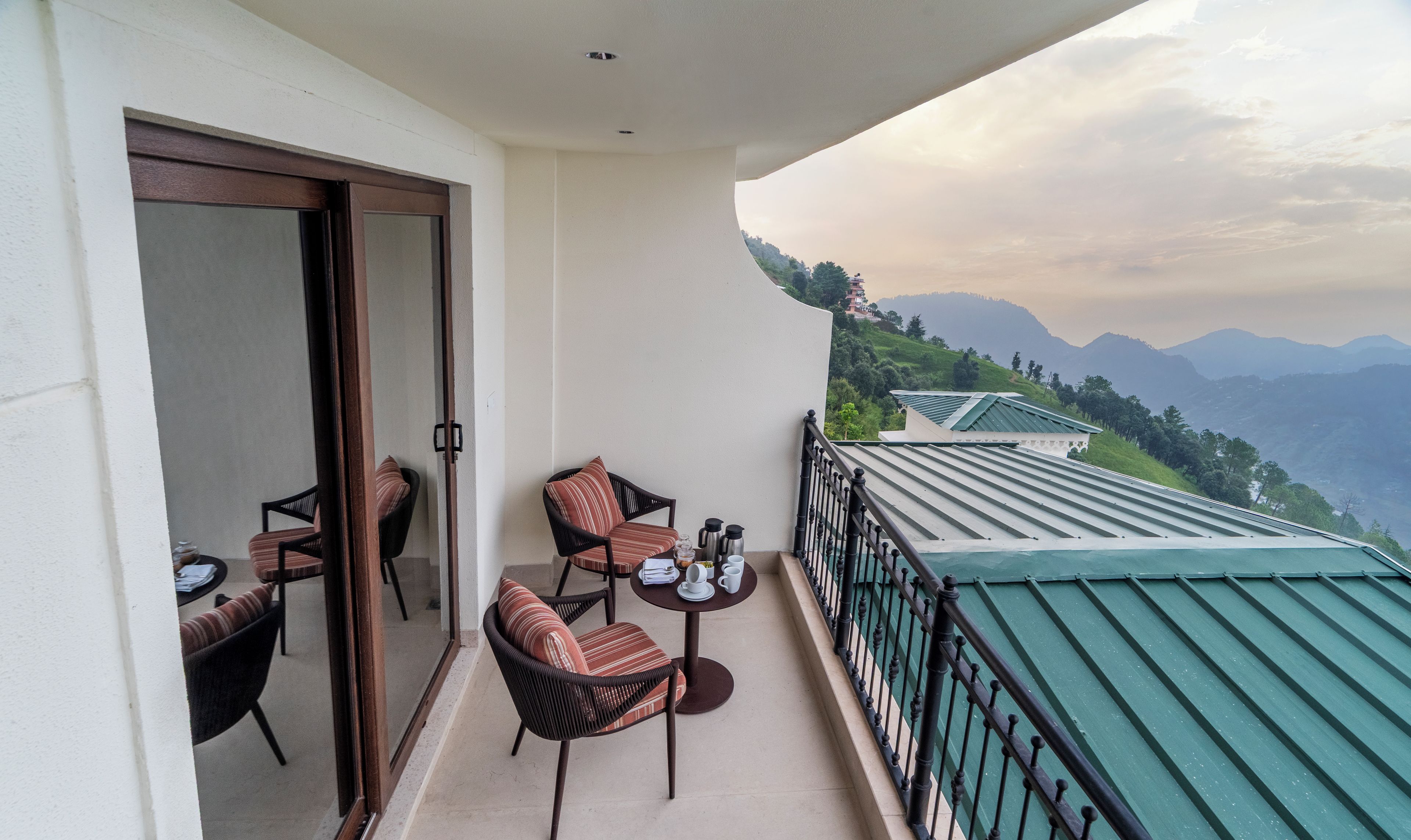 A balcony with two chairs and a table, overlooking a mountainous landscape.