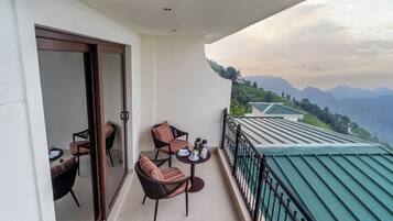 A balcony with two chairs and a table, overlooking a mountainous landscape.
