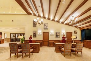 A spacious lobby with a high ceiling, wooden beams, and a chandelier. There are two receptionists standing by a reception desk. - Aurika Naldehra Shimla (Suni)