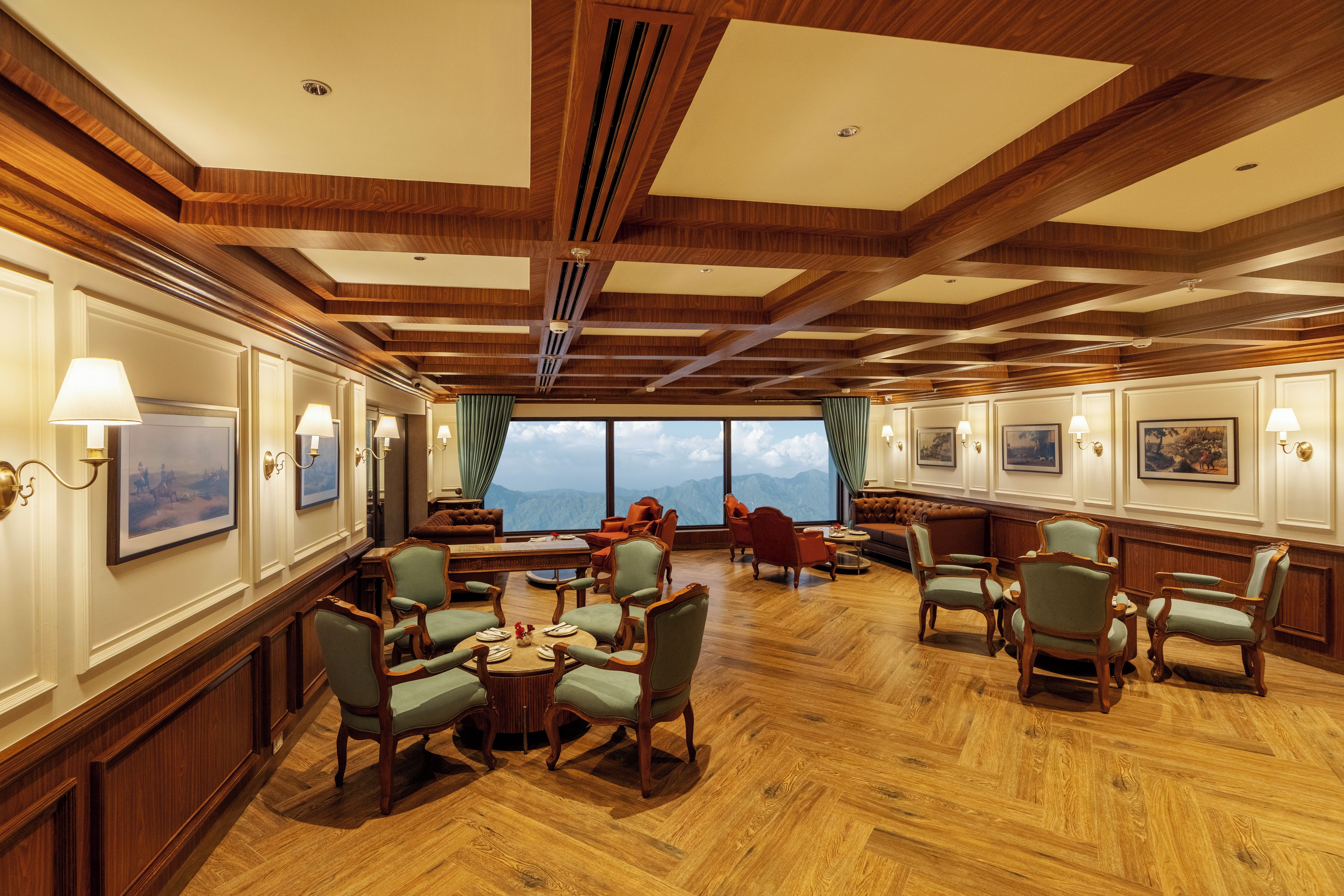 A spacious room with wooden flooring, multiple seating arrangements, and large windows offering a mountain view.