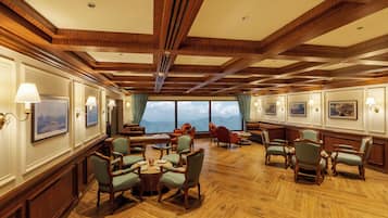 A spacious room with wooden flooring, multiple seating arrangements, and large windows offering a mountain view.
