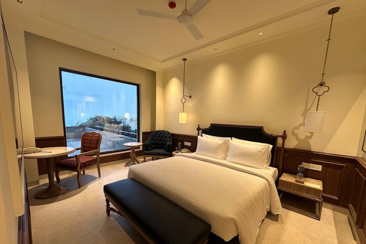 Een hotelkamer met een groot bed, een bureau, een stoel, een bankje en uitzicht op het groen.