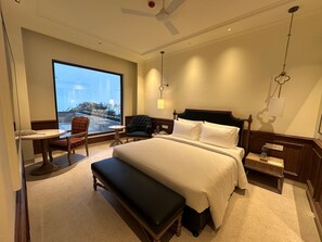 Een hotelkamer met een groot bed, een bureau, een stoel, een bankje en uitzicht op het groen.