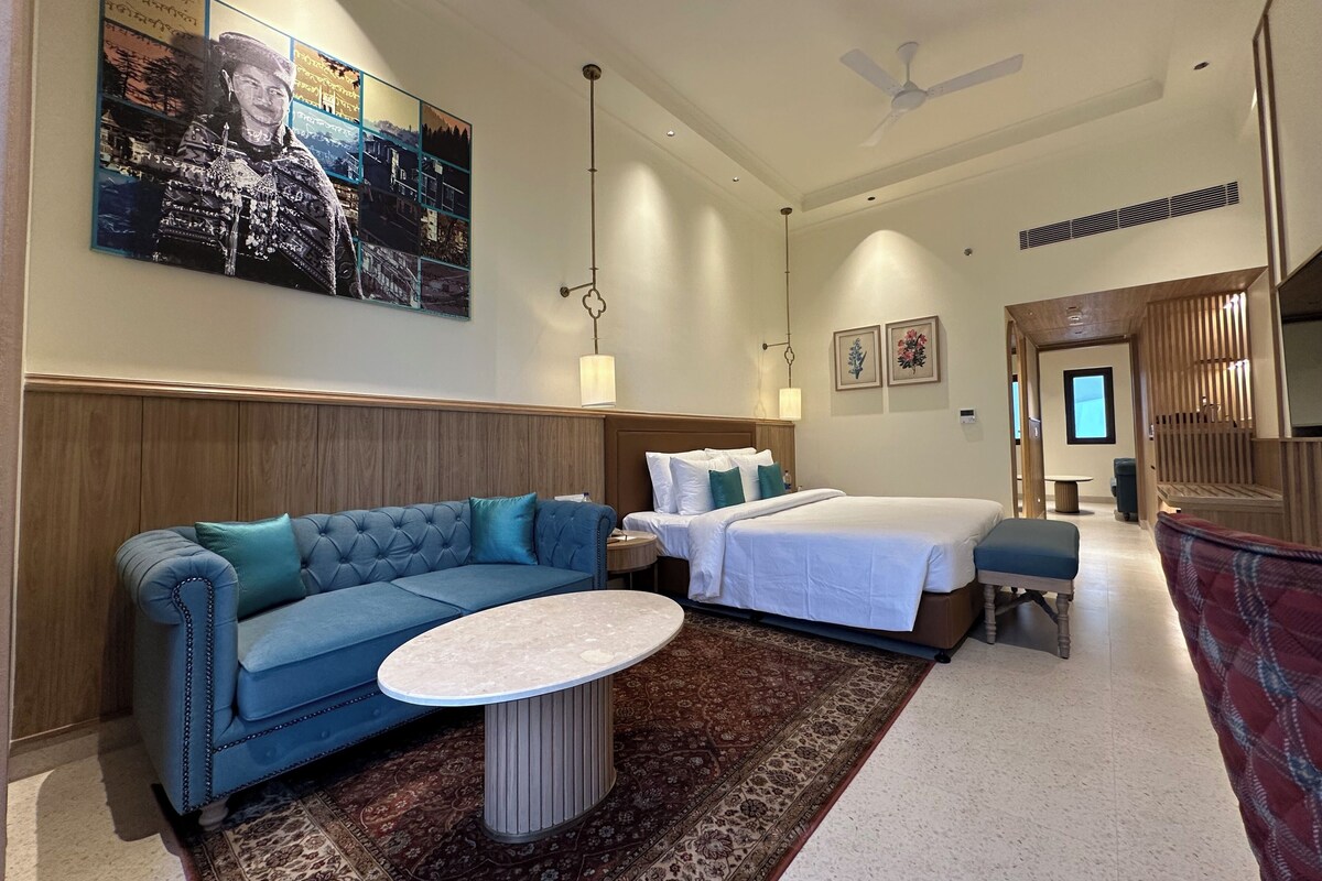 Een hotelkamer met een bed, een slaapbank, een klein tafeltje, een decoratief vloerkleed en een groot kunstwerk aan de muur.