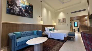 Quarto de hotel com cama, sofá, mesa pequena, tapete decorativo e uma grande obra de arte na parede.