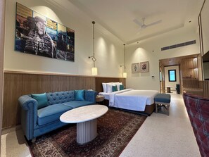 A hotel room with a bed, a sofa, a small table, a decorative rug, and a large wall art piece.