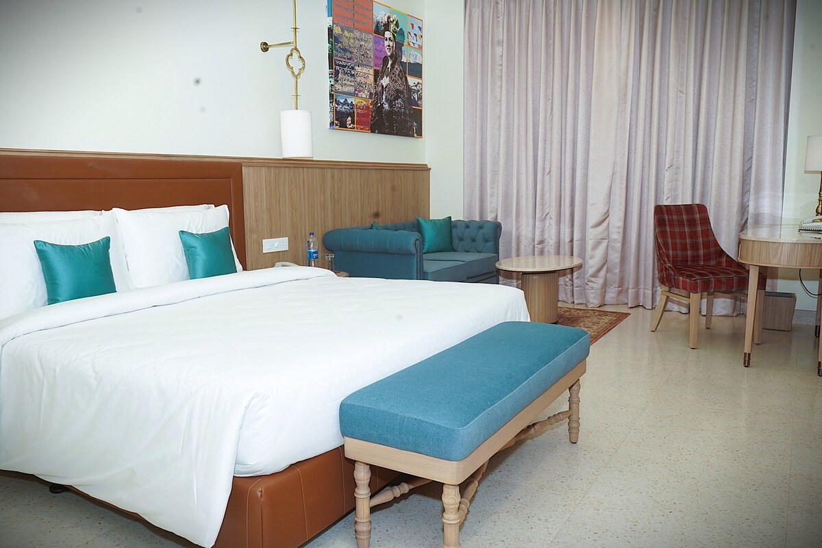 Een hotelkamer met een groot bed, een bankje, een sofa, een bijzettafeltje en een stoel.