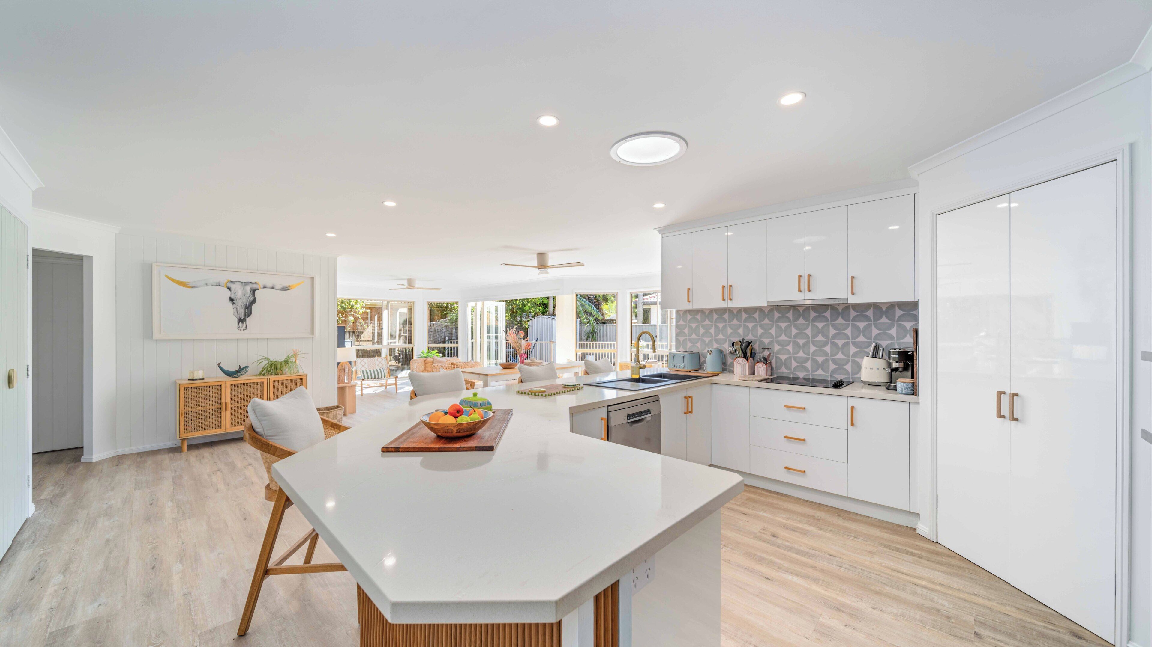 A modern kitchen with white cabinetry, a central island, and a dining area with a view to the outdoors.