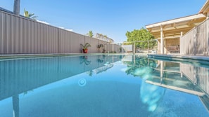 Una piscina cristalina con valla metálica, plantas en macetas y un área de estar cubierta.