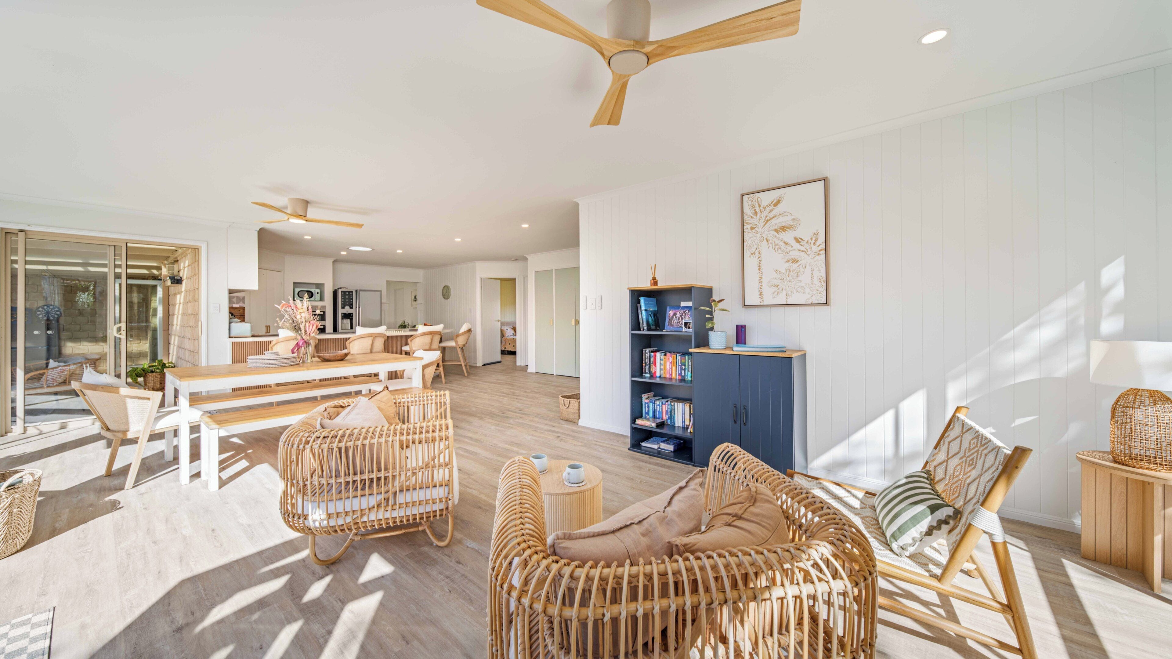 Un vaste espace de vie comprenant une table à manger, des meubles en osier, une bibliothèque et un ventilateur de plafond.