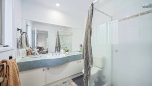 Uma casa de banho moderna com cabine de duche em vidro, um espelho grande e toucador com bancada em granito.