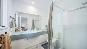 Un baño moderno con cabina de ducha de vidrio, un espejo grande y un mueble de tocador con encimera de granito.