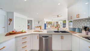 Una cocina moderna con armarios blancos, lavavajillas de acero inoxidable y una zona de comedor con mesa y sillas.