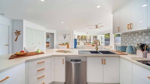 A modern kitchen with white cabinetry, a stainless steel dishwasher, and a dining area with a table and chairs.