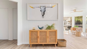 A room with a rattan console, a framed artwork of a bull's head, and a wicker basket. - Salt & Sand Beach House - 6 bedrooms (Ocean Shores)