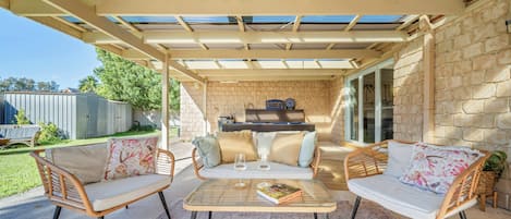 An outdoor patio with a pool table, two wicker chairs, a glass table, and a barbecue grill.