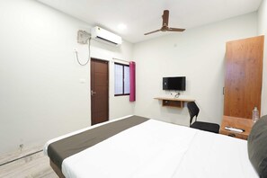 A hotel room with a bed, a desk with a chair, a television, an air conditioning unit, and a wardrobe. - Villa Tian by Palette Homes (Chennai)