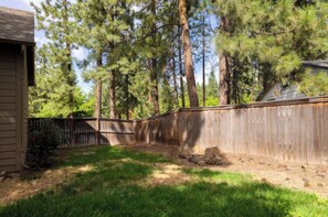 A fenced backyard with a wooden deck, a small pond, and tall pine trees. - Bend Hideaway • Near Mt. Bachelor + Breweries | Hollygrape Pedal & Pine Hideaway (Bend)
