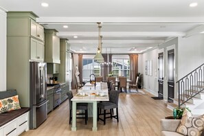 A modern kitchen with a dining area, wooden flooring, and a staircase. - Private Infinity Pool + Elevator + Pool Table | Steps to Sand | Boardwalk & Blue (Hilton Head Island)