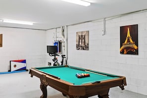 A pool table with a green felt surface, a pool cue, and several balls. There are two posters on the wall, one of a bridge and another of the Eiffel Tower. - Private Infinity Pool + Elevator + Pool Table | Steps to Sand | Boardwalk & Blue (Hilton Head Island)