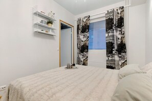 A bedroom with a bed, a window with curtains, a door, and a shelf with items. - Nordic Heart Apartment, Sauna By Lapland Host (Rovaniemi)
