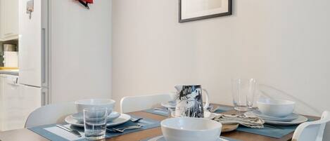 A dining table set with plates, bowls, glasses, and cutlery, with a framed picture on the wall and a fire extinguisher on the wall.