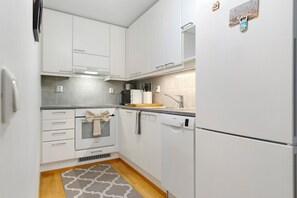 A compact kitchen with white cabinetry, a built-in oven, a dishwasher, and a refrigerator. - Nordic Heart Apartment, Sauna By Lapland Host (Rovaniemi)
