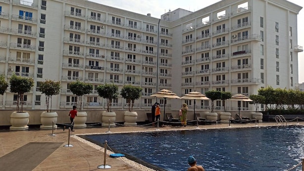 A hotel with a swimming pool, multiple balconies, and outdoor seating areas. - Luxury Apartments Stay at DLF (Lucknow)