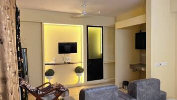 A modern hotel room with a large bed, a seating area with sofas, a television, and a ceiling fan.