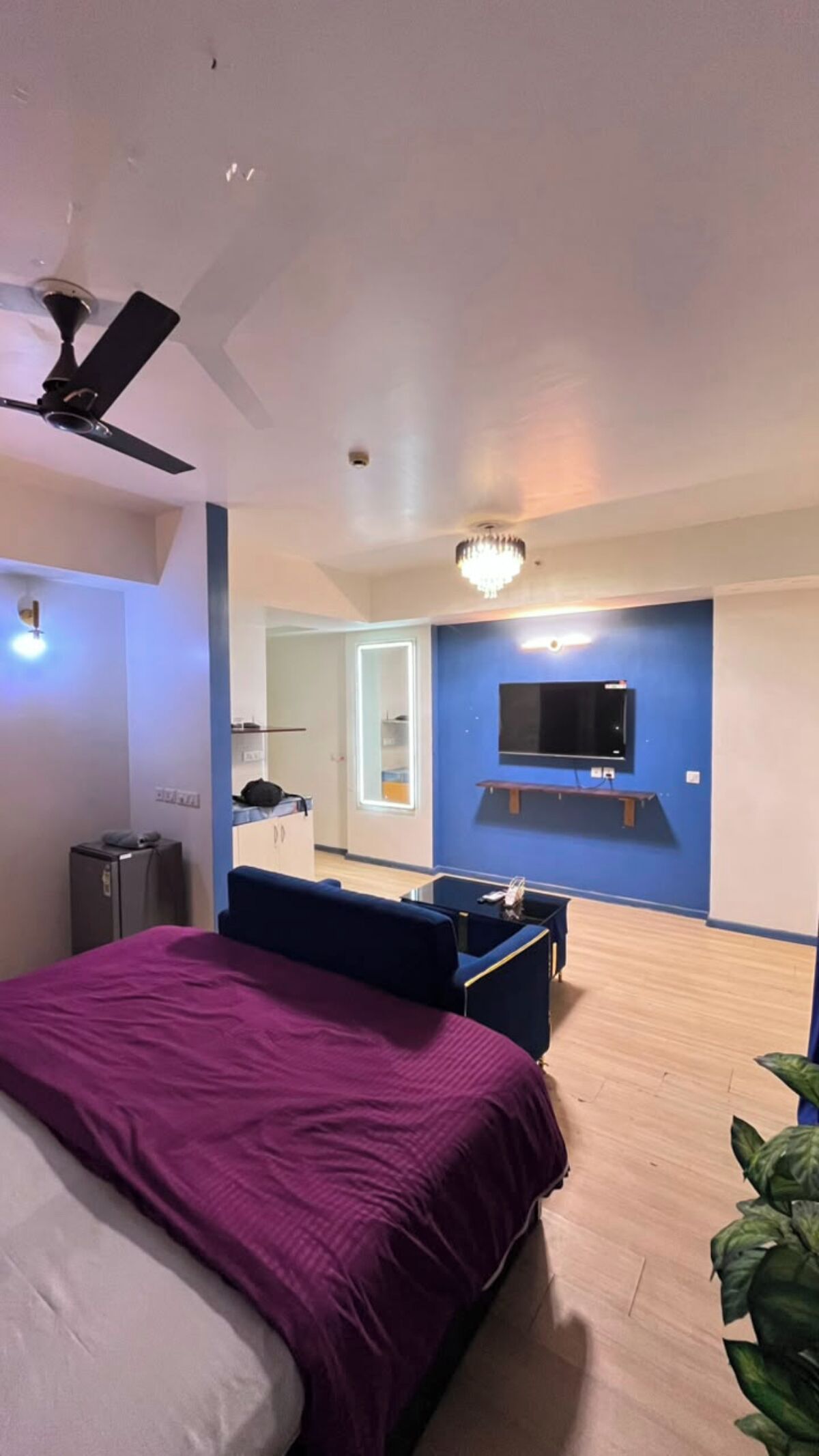 A bedroom with a bed, a ceiling fan, a TV, and a small table.