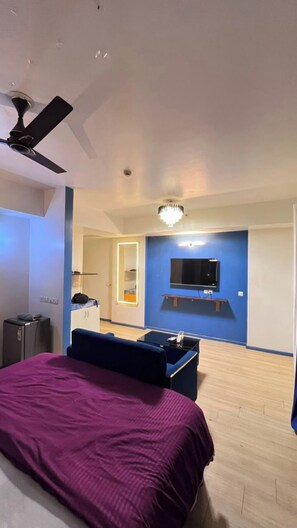 Une chambre à coucher avec un lit, un ventilateur de plafond, un téléviseur fixé au mur et une petite table.