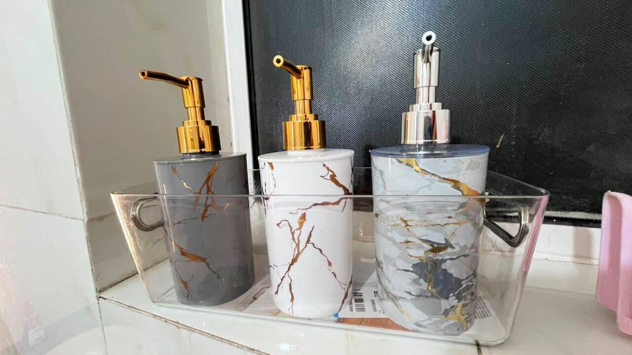 Drie zeepdispensers in transparante verpakkingen met gouden pompen, geplaatst op een plank.