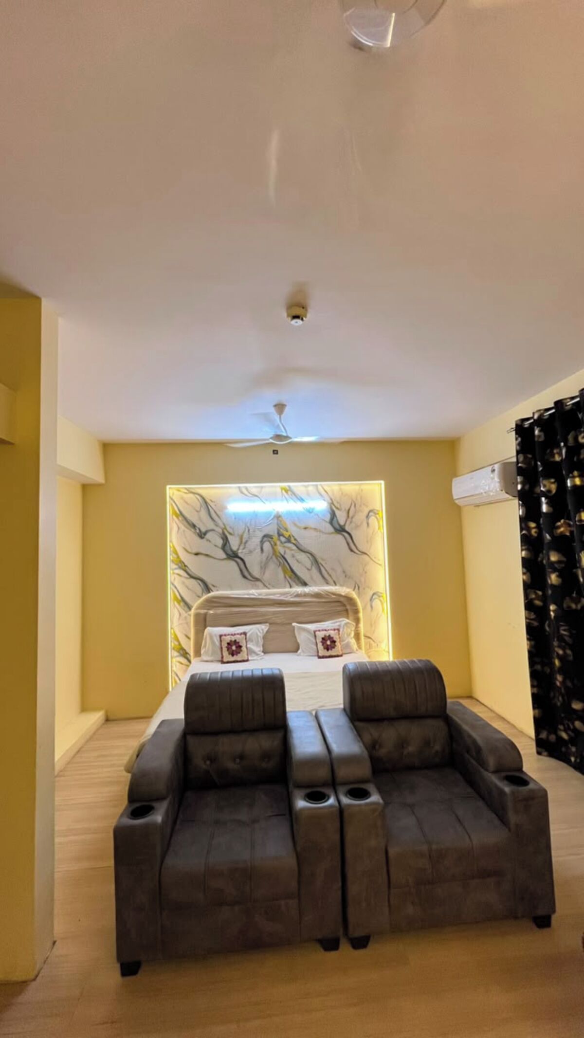 Una stanza con un letto, due poltrone, una ventola a soffitto e un condizionatore d'aria a parete.