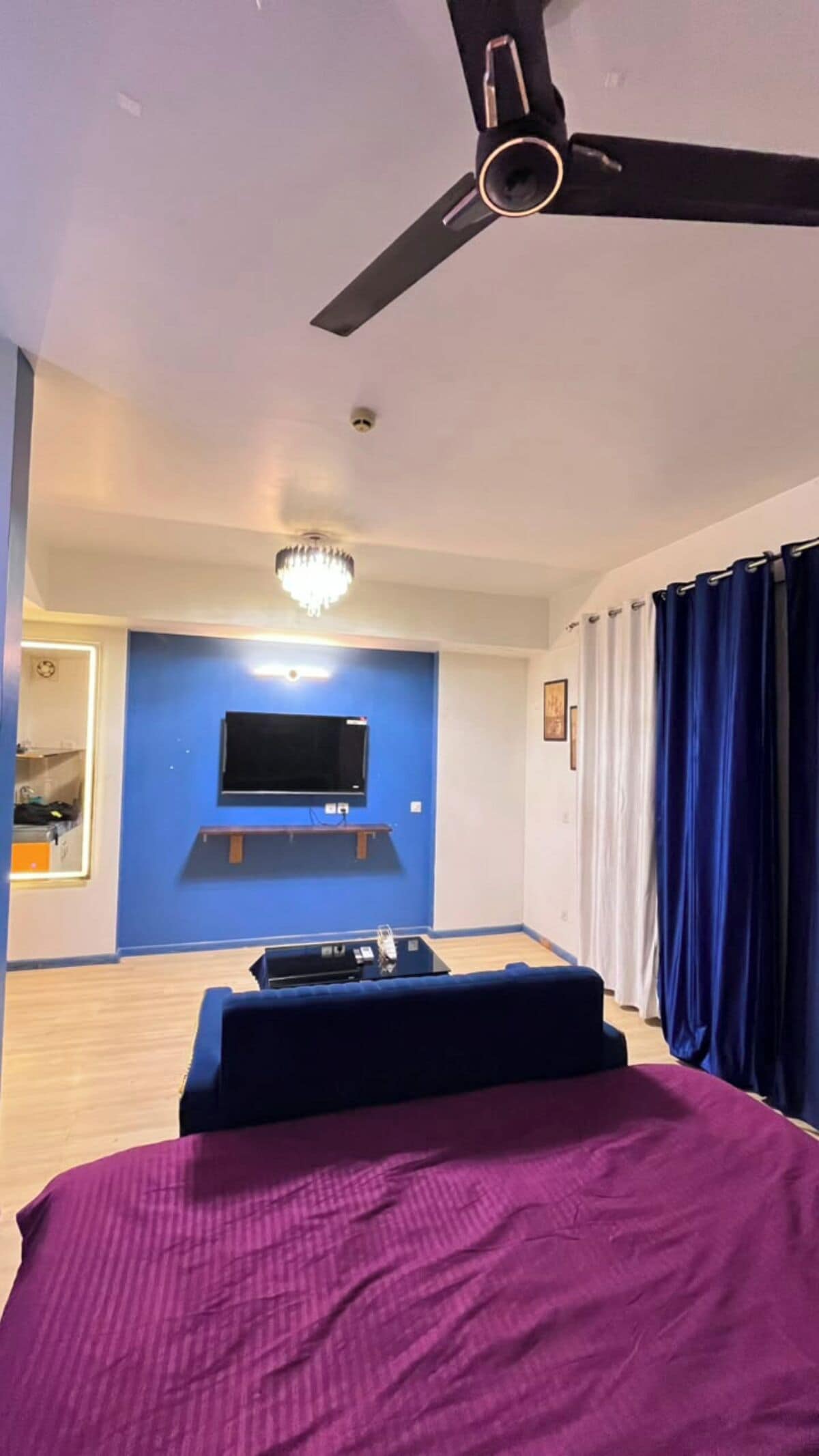 Une chambre à coucher avec un lit, un ventilateur de plafond, un téléviseur fixé au mur et un lustre.