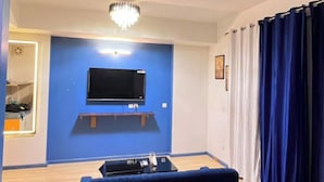 A bedroom with a bed, a ceiling fan, a mounted TV, and a chandelier. - Luxury Apartments Stay at DLF (Lucknow)