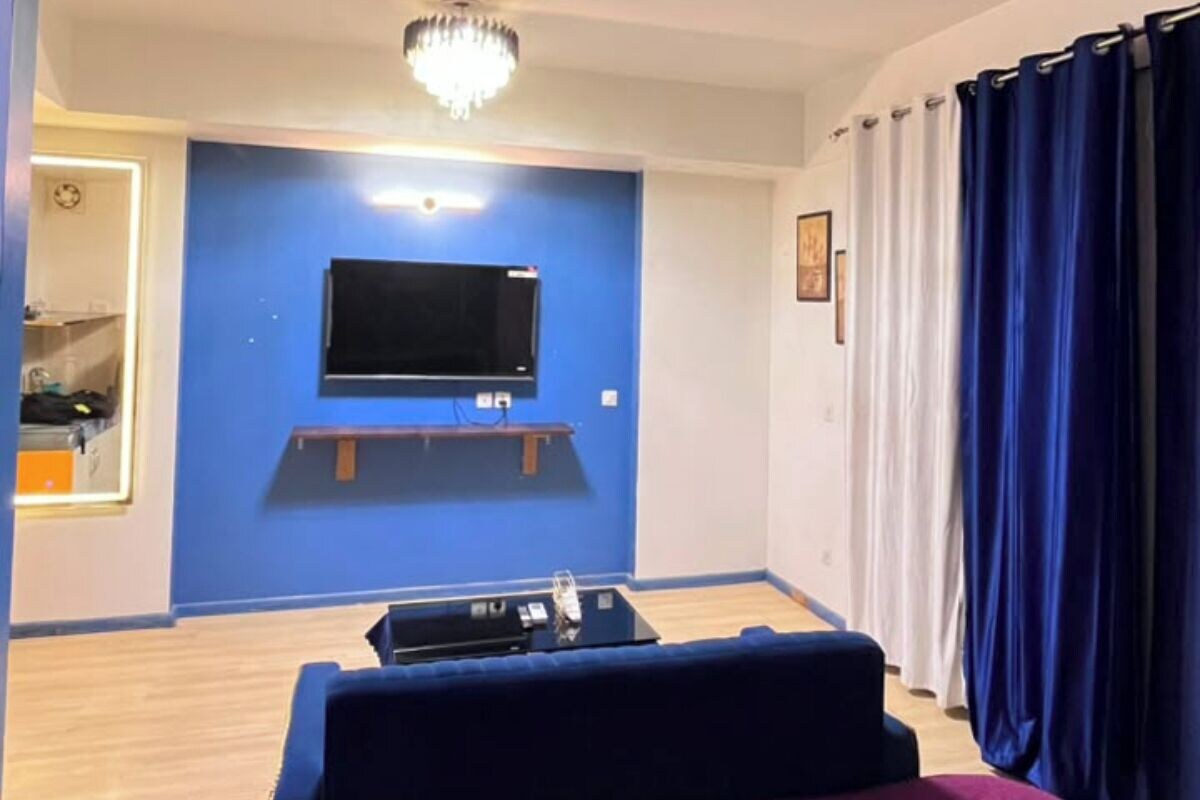 Une chambre à coucher avec un lit, un ventilateur de plafond, un téléviseur fixé au mur et un lustre.