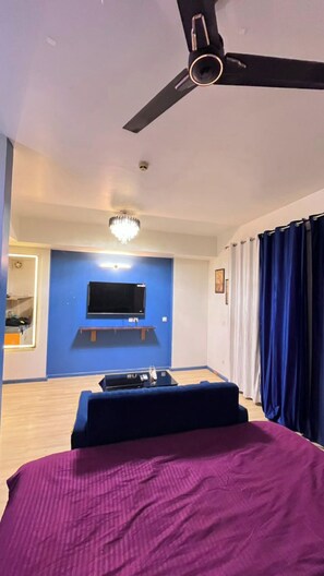 Une chambre à coucher avec un lit, un ventilateur de plafond, un téléviseur fixé au mur et un lustre.