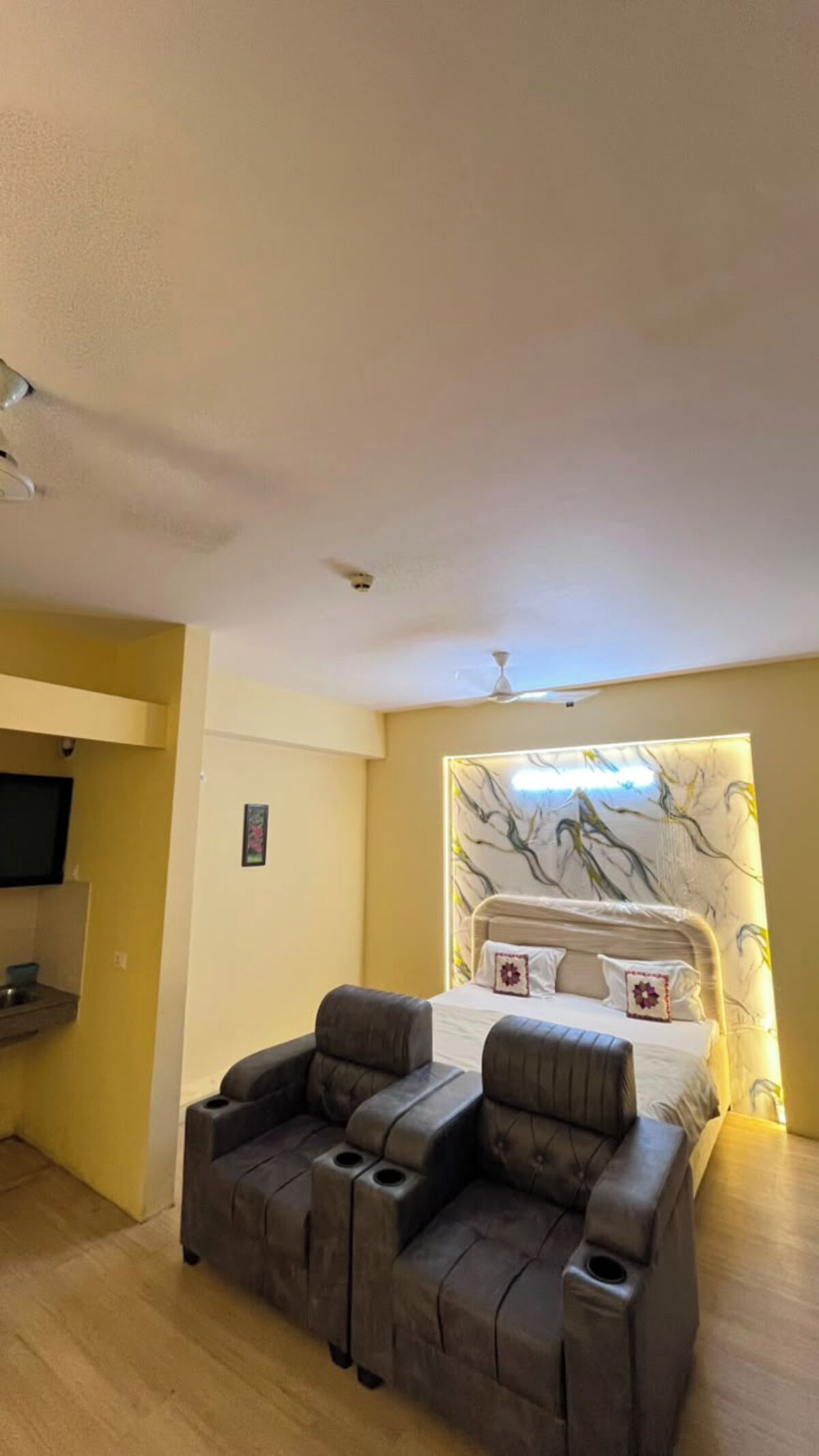 A bedroom with a bed, a sofa, a ceiling fan, and a wall-mounted TV.