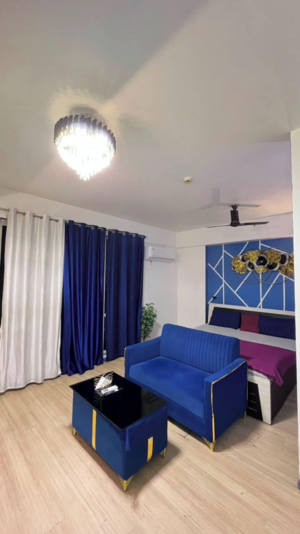 Un salon avec un canapé bleu, une table basse noire et un luminaire suspendu au plafond.