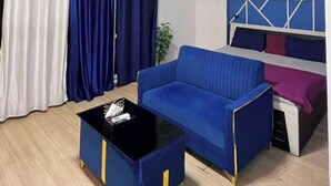 A living room with a blue sofa, a black coffee table, and a ceiling light fixture. - Luxury Apartments Stay at DLF (Lucknow)