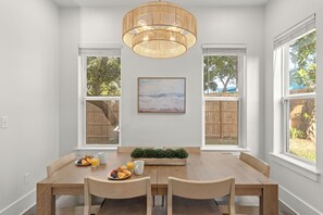 A dining area with a wooden table, chairs, a fruit plate, a coffee mug, and a painting on the wall. - Golf Cart + Game Room + Pool Access | Steps to the Sand | Sundrift (Miramar Beach)