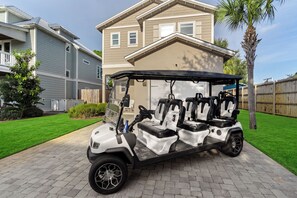A golf cart parked on a paved driveway with a house in the background. - Golf Cart + Game Room + Pool Access | Steps to the Sand | Sundrift (Miramar Beach)