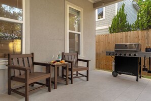 Un patio al aire libre con dos sillas de madera, una mesa con comida y bebidas, y una parrilla portátil.
