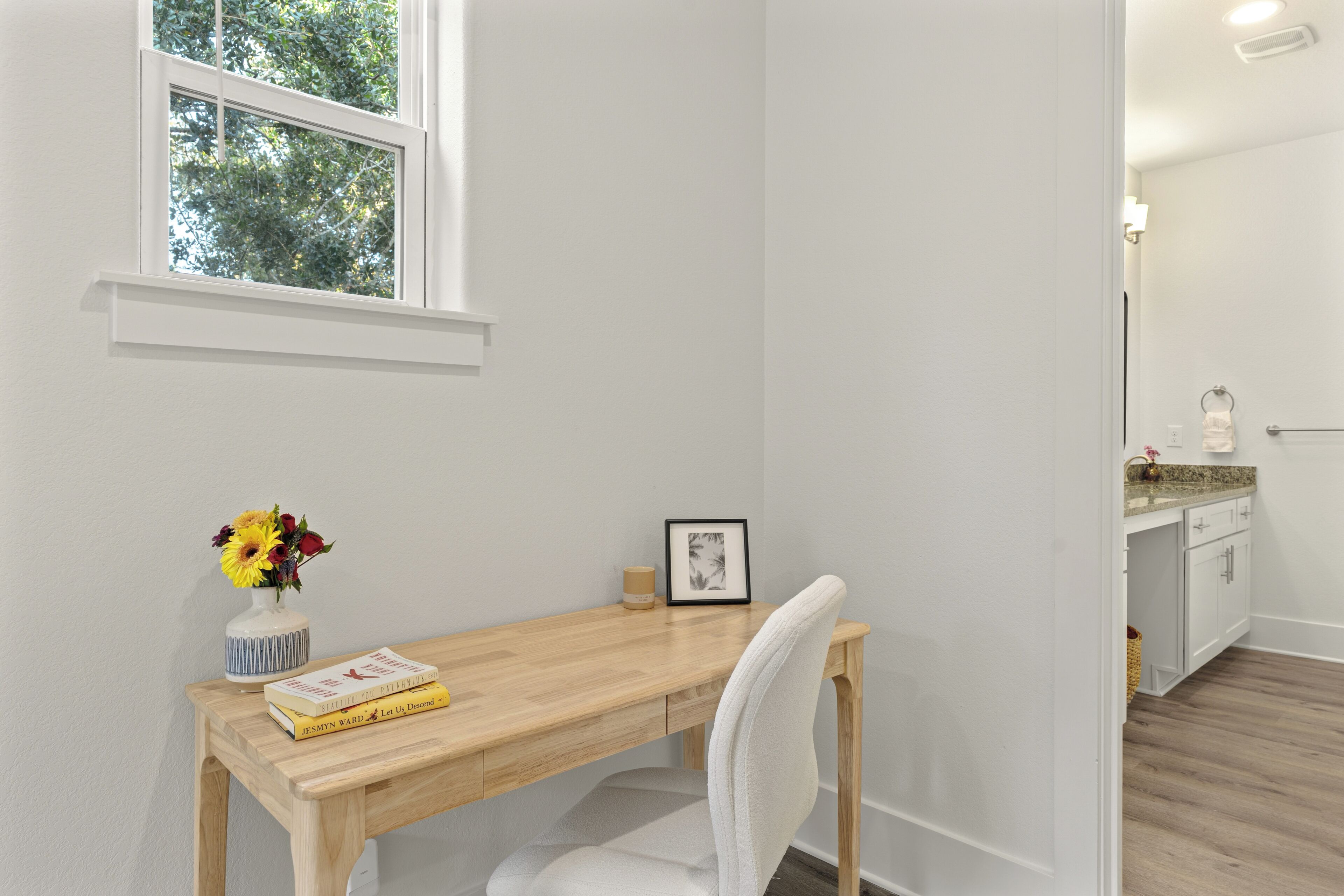 A study room with a wooden desk, a chair, a vase with flowers, and a framed picture on the wall.