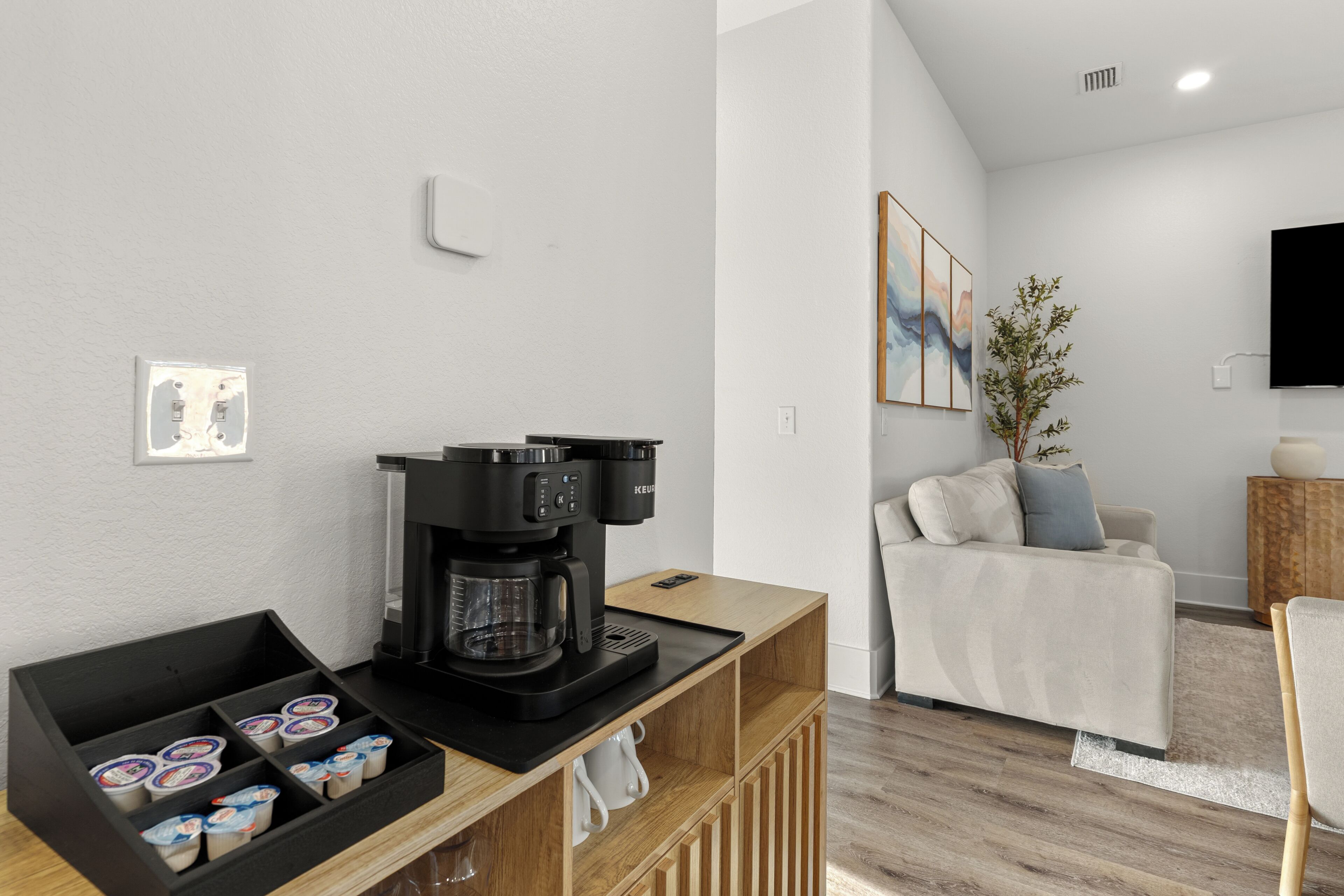 A modern living room with a coffee machine, a sofa, a TV, and a plant.