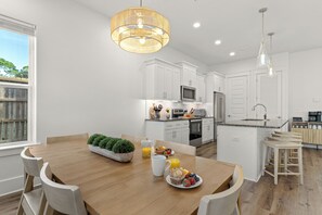 Una cocina moderna con armarios blancos, una mesa de comedor de madera y una preparación para el desayuno con frutas y jugo.