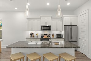 Eine moderne Küche mit weißen Schränken, Edelstahlgeräten, einer Granitabdeckung und Holzbarhocker.